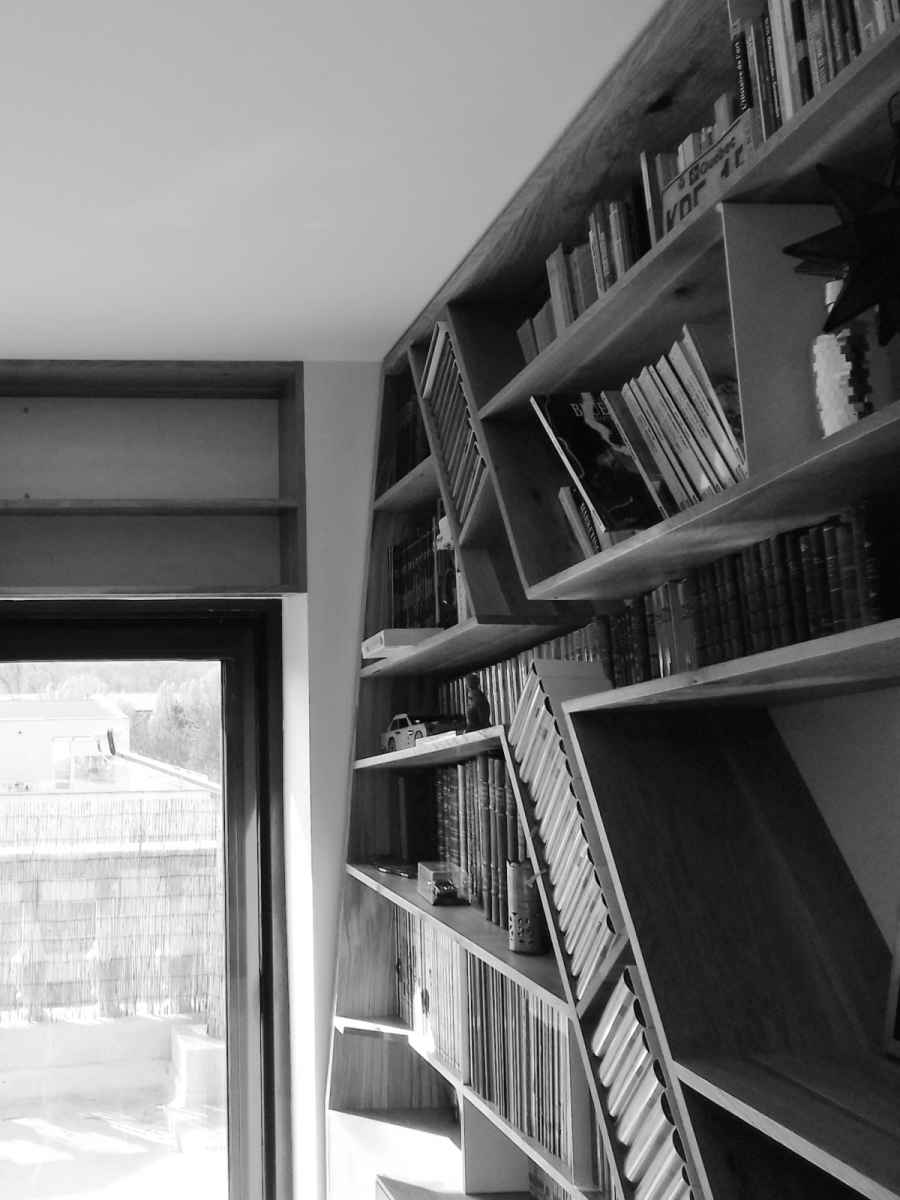 Detaliu de colț cu biblioteca instalată în care se observă rafturile înclinate pentru cărți