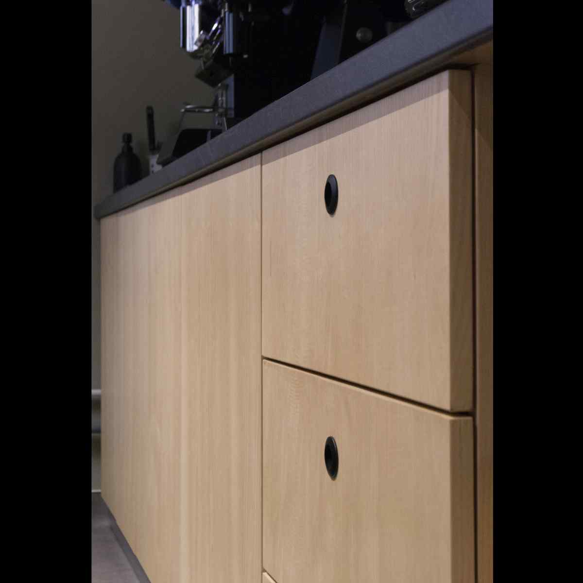 Detaliu fronturi furniruite cu mânere îngropate rotunde în interiorul cafenelei