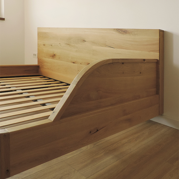 Pat din lemn masiv la nuanta nucului, cu colturi rotunjite, cu tablie formata din panouri decorative aplicate pe de perete, si noptiere suspendate