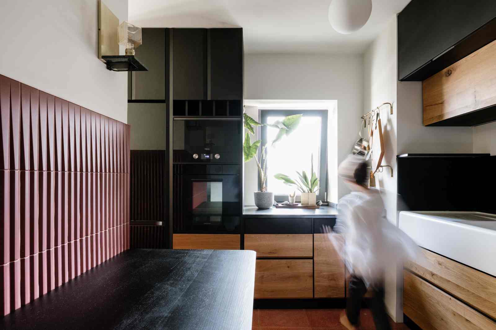 Bucatarie cu masa neagra din lemn si corpuri de mobilier inalte si joase cu usi din lemn de stejar masiv alternate cu usi negre din placaj vopsit.