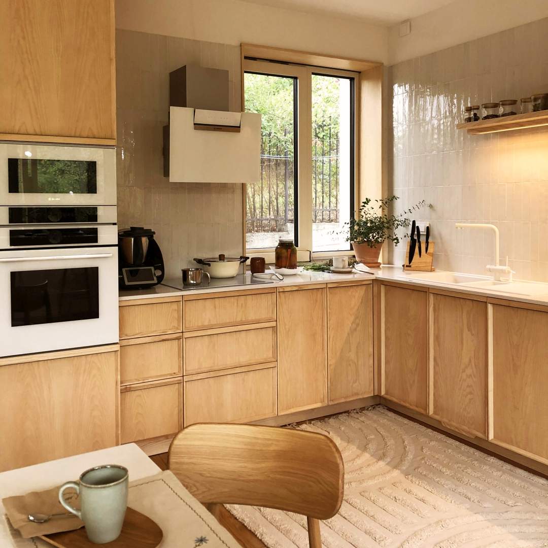 bucatarie in nuanta deschisa din lemn de frasin cu dulap inalt, corpuri joase cu blat alb, cu usi cu rame